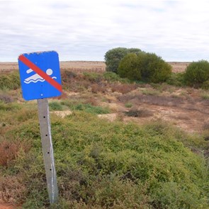 Warning sign at the earthen tank near the yellow bus