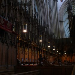 The dimly lit Quire, all ancient burnished wood.