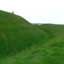 A figure on the skyline gives scale to the ditch and bank at Maiden Castle.